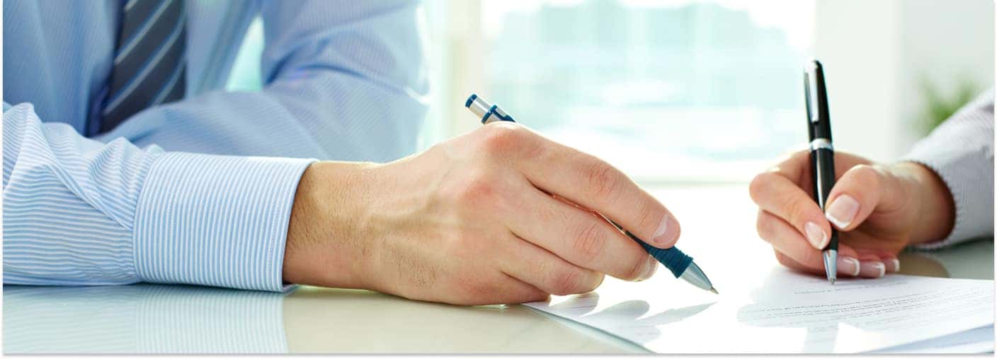 Close-up of a customer signing auto financing paperwork with a representative.