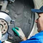 car mechanic worker replacing brakes of lifted automobile at auto repair garage shop station