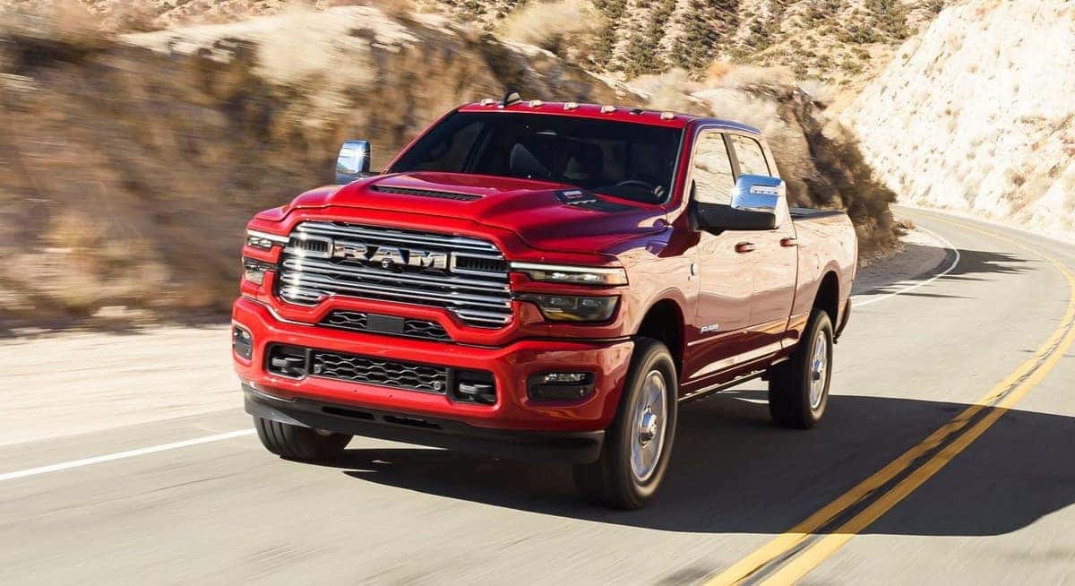 A red RAM 2500 truck driving on a winding desert highway, showcasing its power and rugged design. Available at Bernard Northtown.