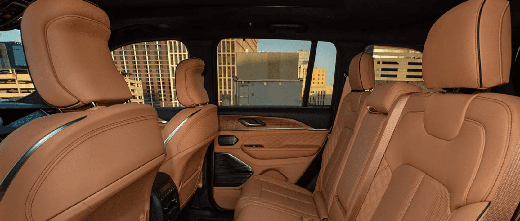 Interior view of the second-row seating in the 2025 Jeep Grand Cherokee, featuring premium quilted tan leather seats, wood accents on the door panels, and a city skyline visible through the windows.