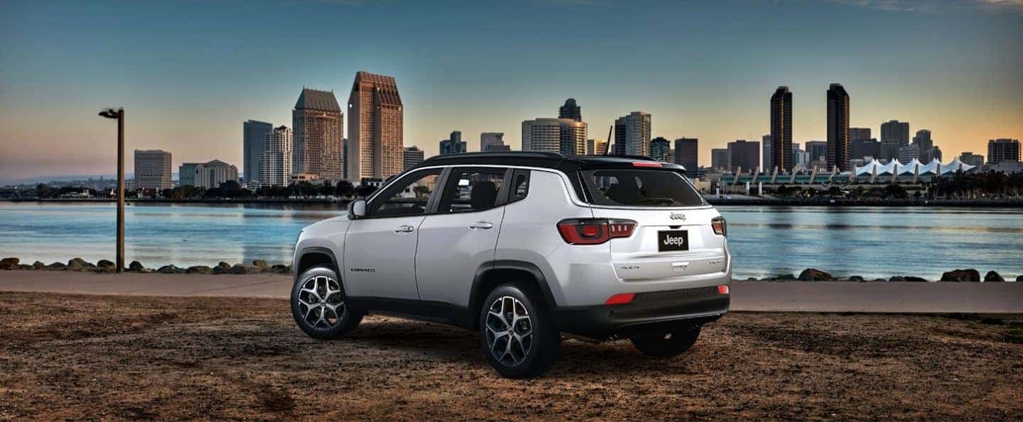 025 Jeep Compass in silver parked near a city waterfront at sunset, showcasing its modern design and urban versatility, available now at Bernard's Northtown Jeep dealership.