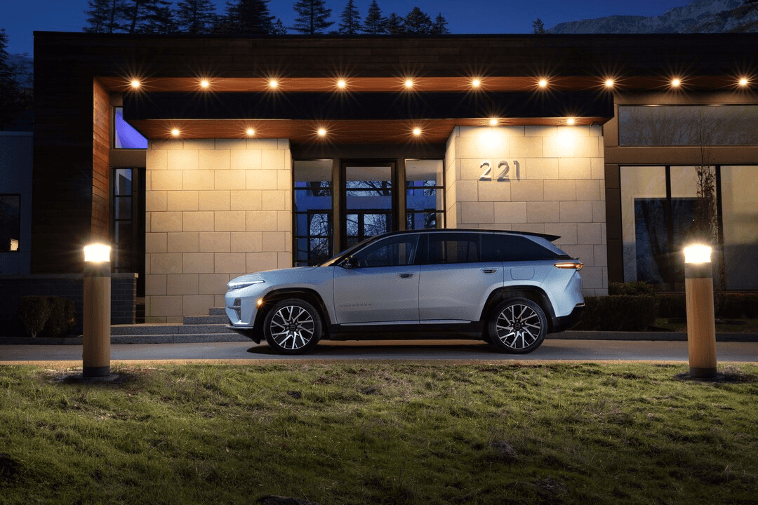 2025 Jeep Wagoneer S in silver parked at night outside a modern, well-lit building, highlighting its sleek SUV profile and luxury styling.