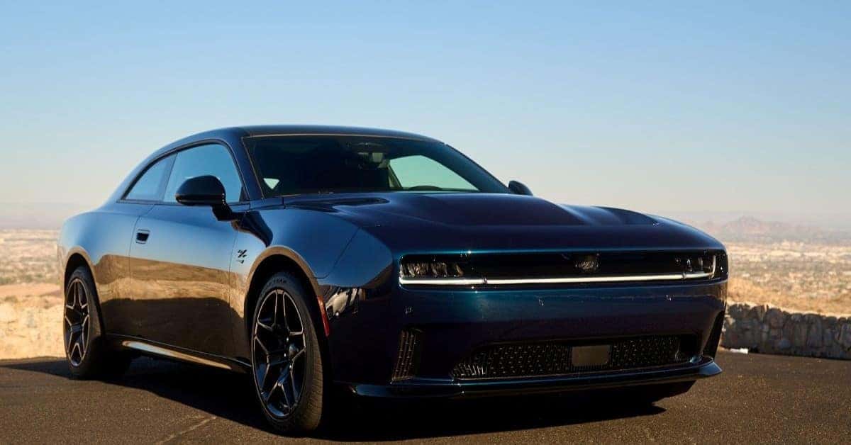 A sleek, dark blue 2025 Dodge Charger EVtwo-door muscle car parked on a scenic overlook at sunset, emphasizing modern performance design.
