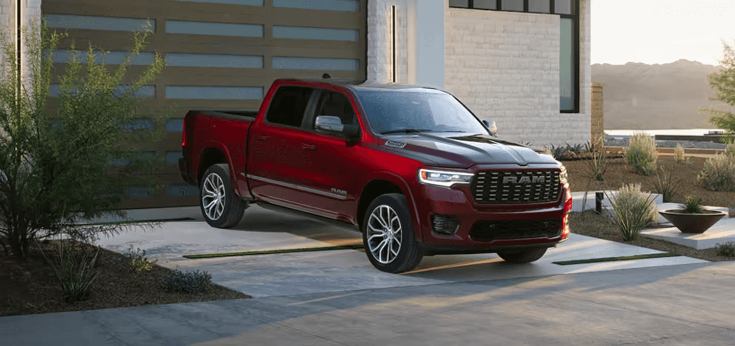 Red RAM 1500 parked in a driveway outside a modern house at sunset.