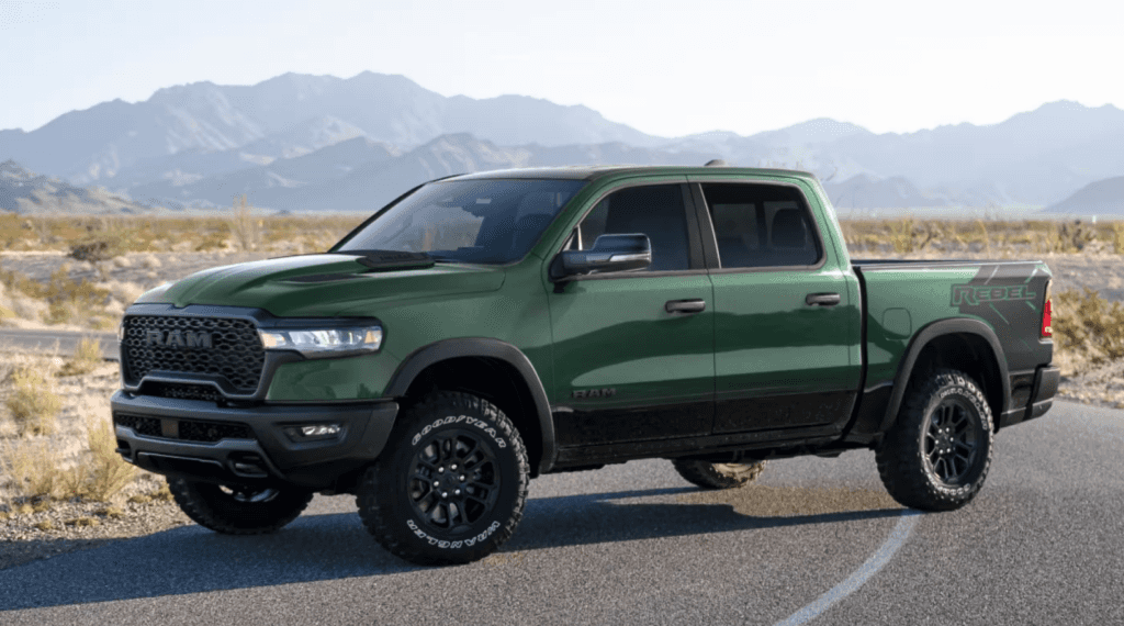 A green RAM Rebel pickup truck parked on a desert road with mountains in the background.