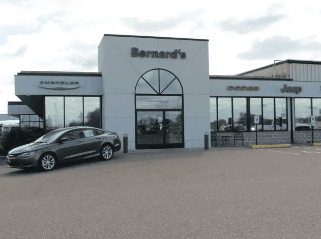 Exterior view of Bernard's Chrysler Dodge Jeep dealership with a gray Chrysler sedan parked out front.
