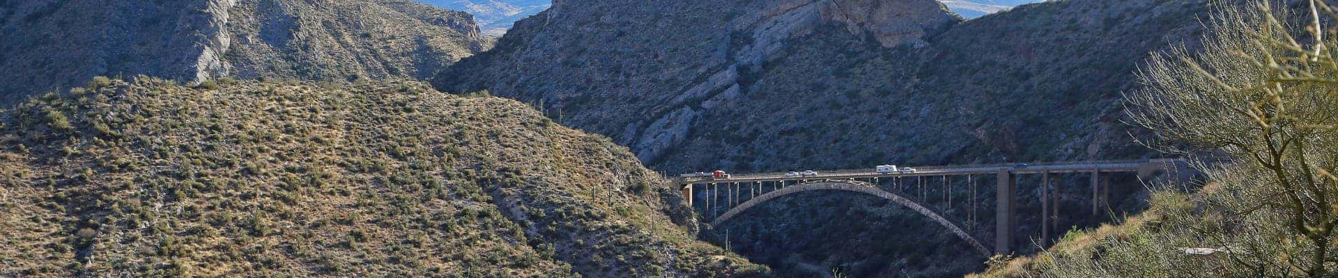 Scenic desert canyon landscape with a bridge spanning a rocky valley, surrounded by rugged hills.
