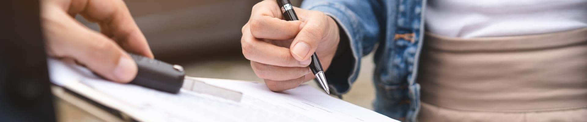 Customer signing paperwork while receiving a vehicle key during the car-buying process.