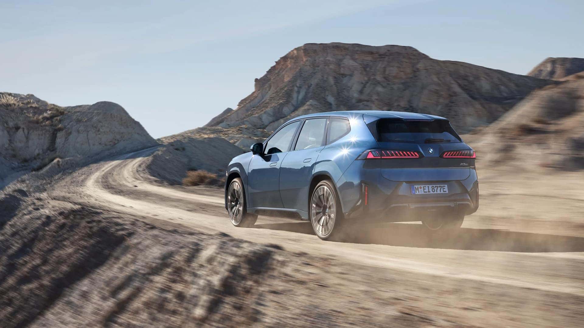 Back view of 2026 BMW iX3 driving on dirt road