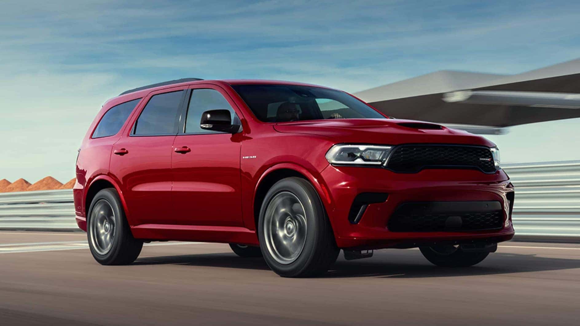 A red Dodge Durango driving through a road near a desert.