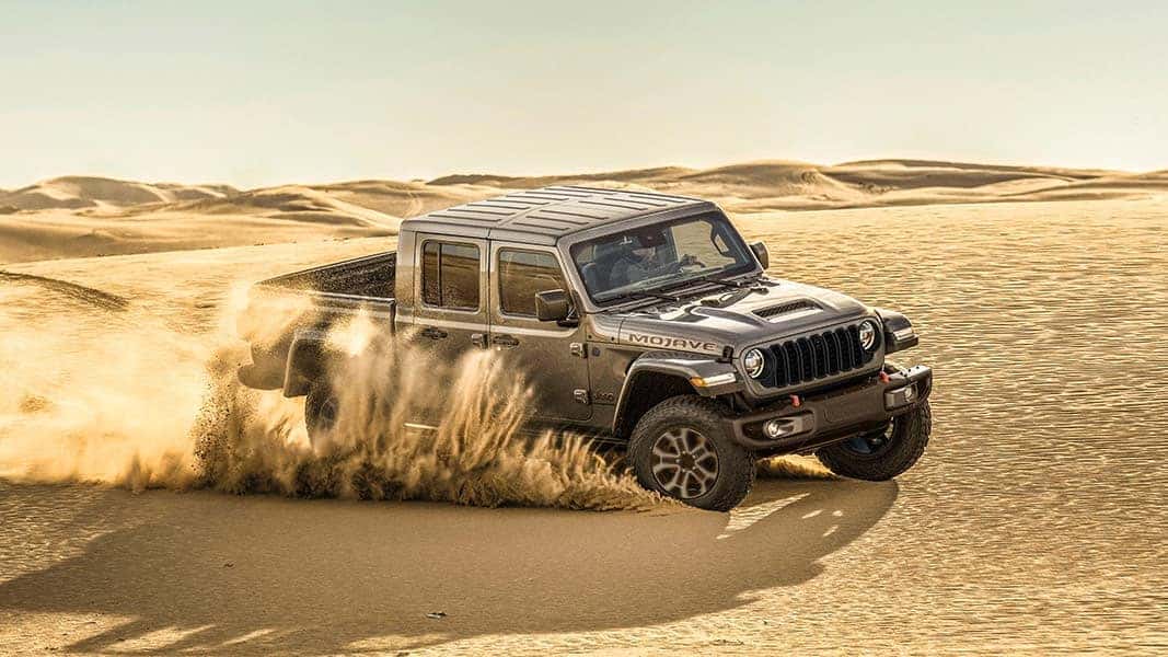 A gray Jeep Gladiator driving through a desert and kicking up sand.