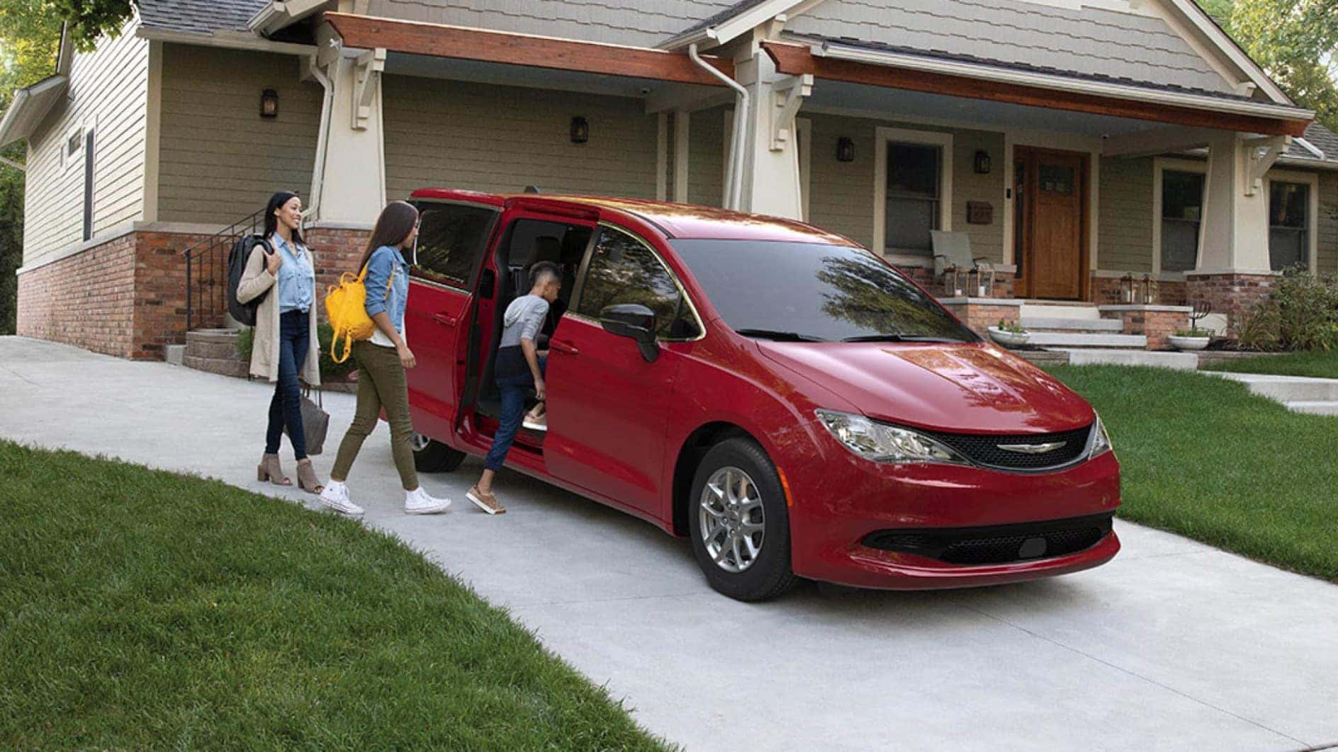 A red Chrysler Voyager sitting in a driveway as a family gets inside.