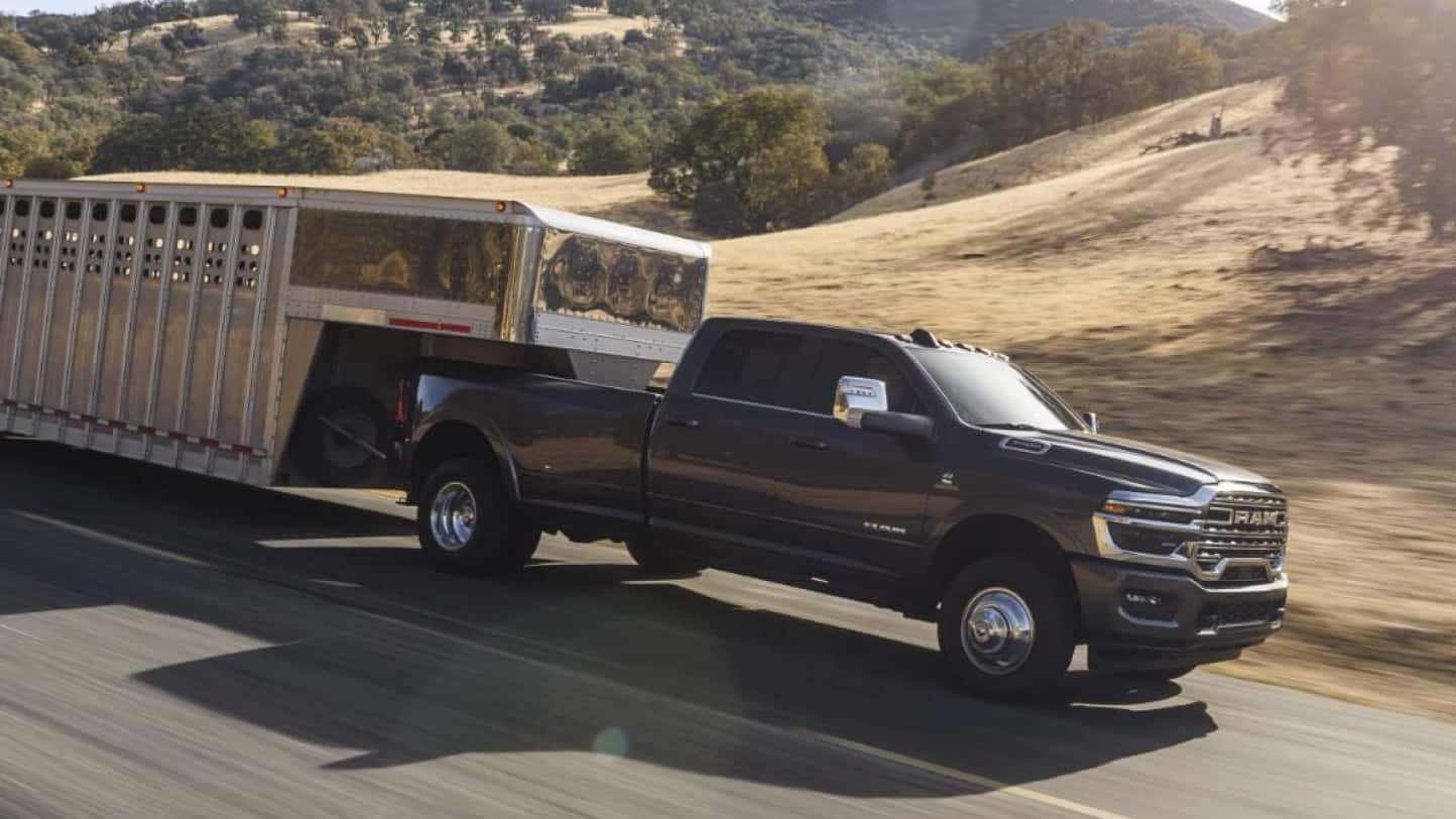 A black RAM 3500 hauling a trailer while driving down the road in a desert.