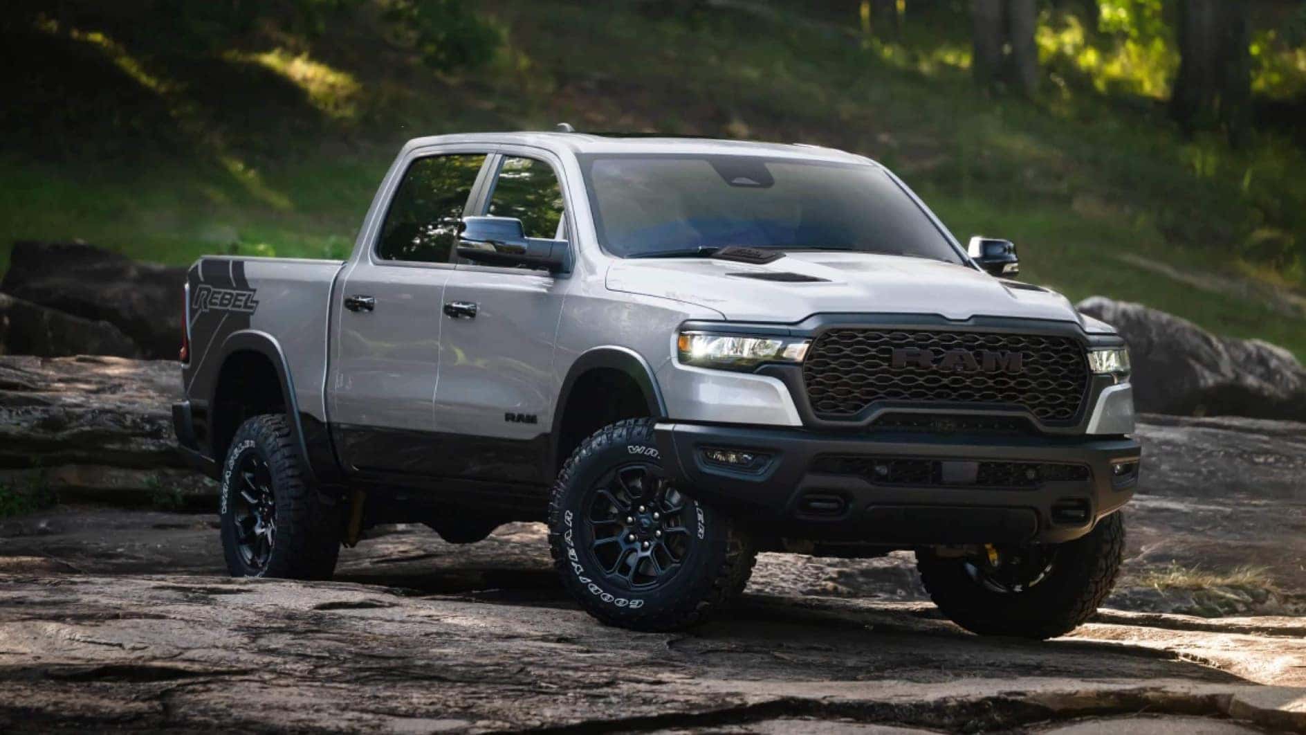 A silver RAM 1500 driving off-road near a forest.