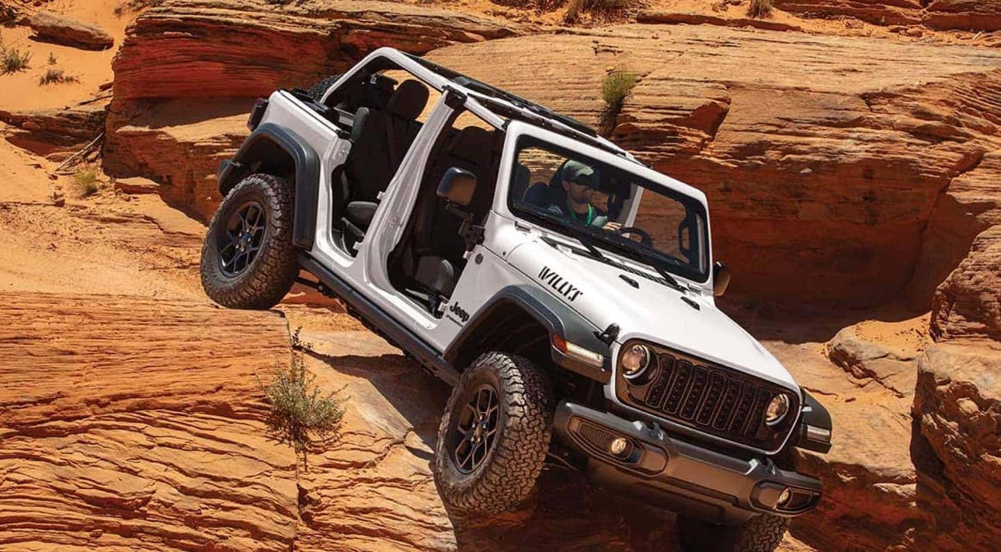 A white Jeep Wrangler driving over rocky terrain.