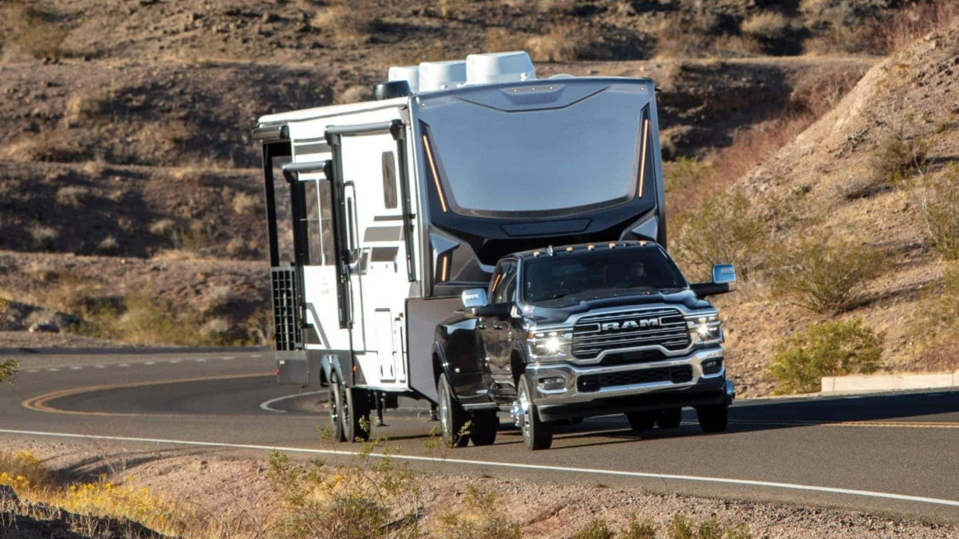 A gray RAM 3500 driving down a road in a desert while towing a large trailer.