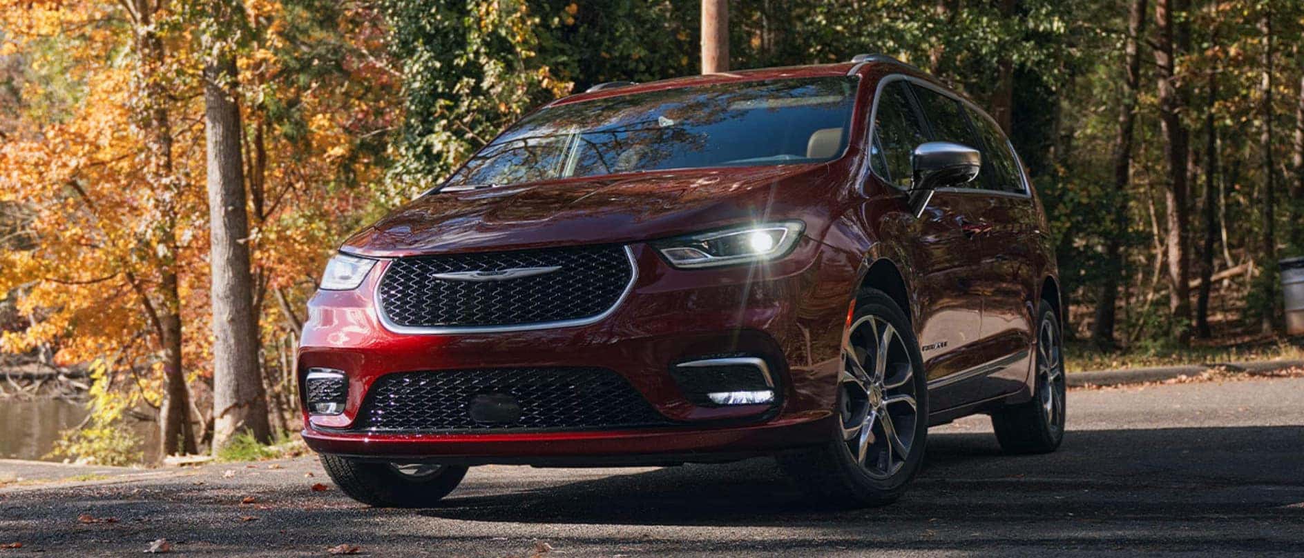 A red Chrysler Pacifica driving on a trail through a forest in autumn.