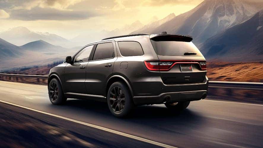 A dark gray Dodge Durango driving on the road by a mountain range.