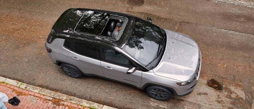 An overhead view of a silver Jeep Compass by the curb with the moonroof open.