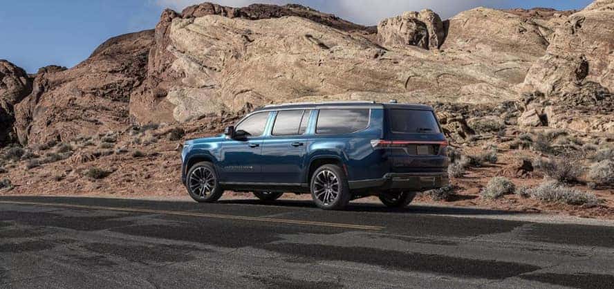 A bleu Jeep Grand Wagoneer stopped by the side of the road in a desert.