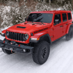 A red Jeep Wrangler driving through snow.