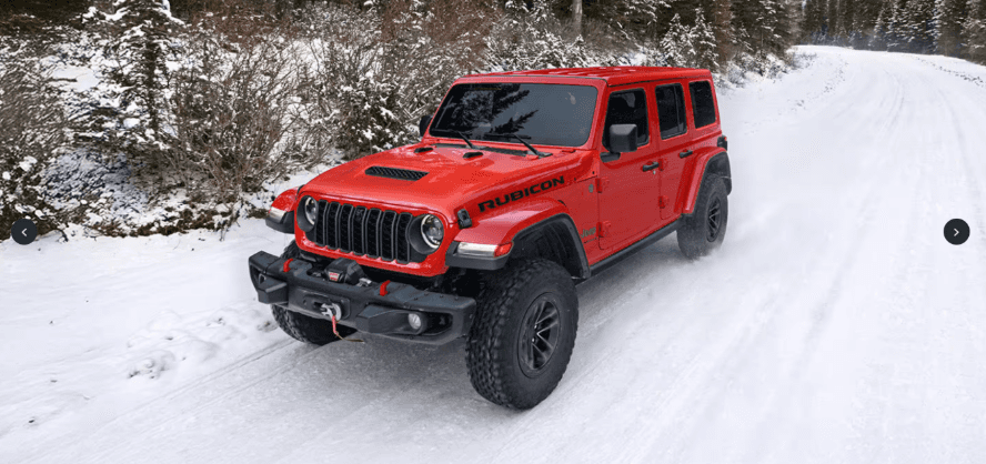 A red Jeep Wrangler driving through snow.