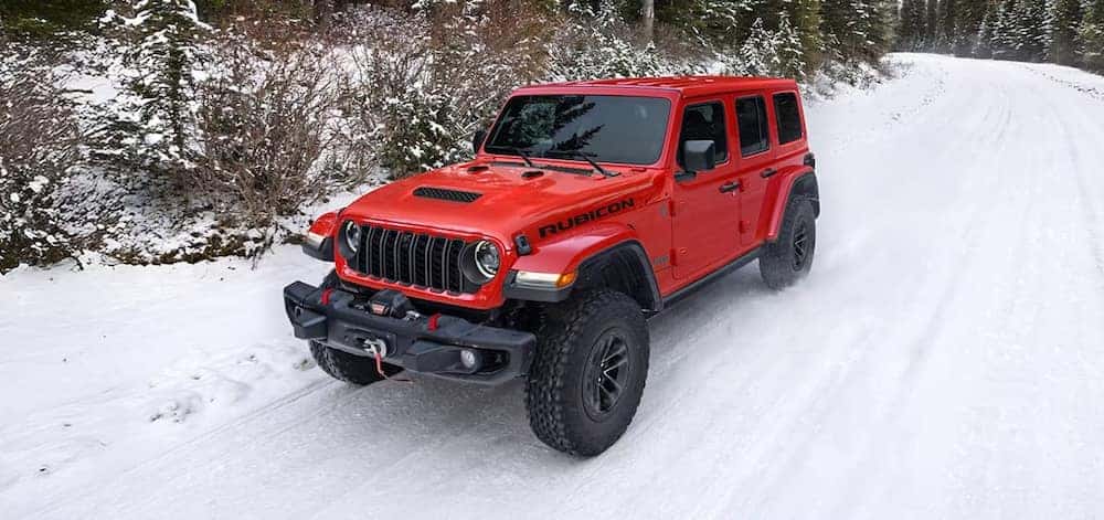  red Jeep Wrangler driving on a snow-covered road or path.