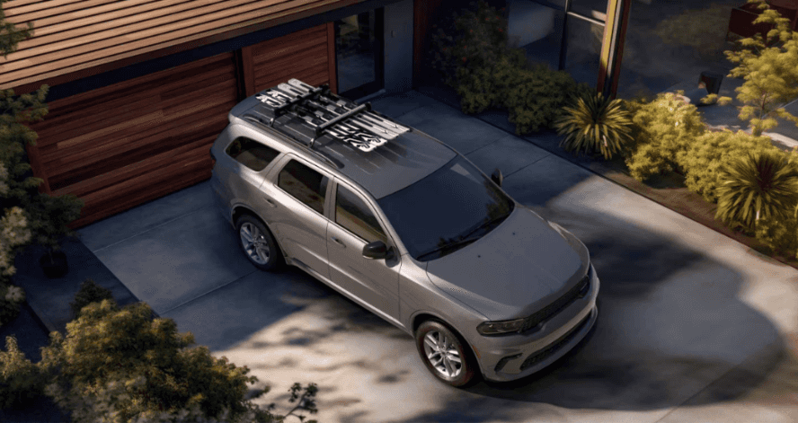 An overhead image of a gray Dodge Durango with skis on the roof in a driveway.