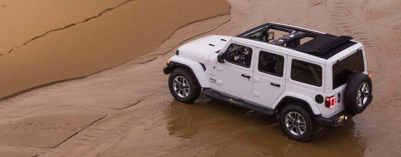 A white 2019 Jeep Wrangler Unlimited with the roof open is shown on a beach from a high angle.