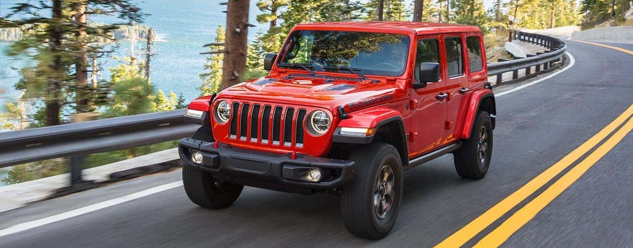 A red 2021 Jeep Wrangler Rubicon is driving past pine trees on a mountain road.