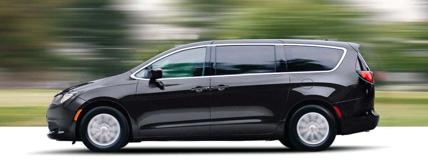 A black 2021 Chrysler Voyager is shown from the side speeding past blurred trees.