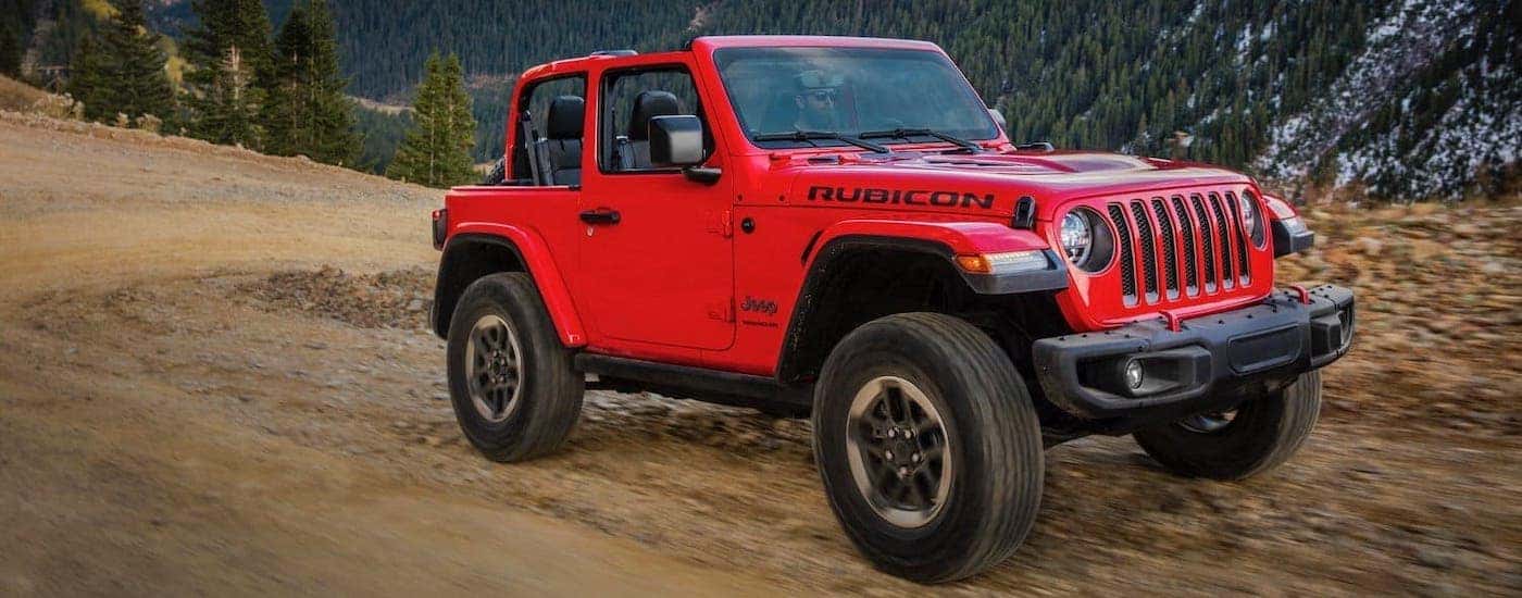 A red 2019 used Jeep Wrangler Rubicon is driving on a dirt trail in the mountains.