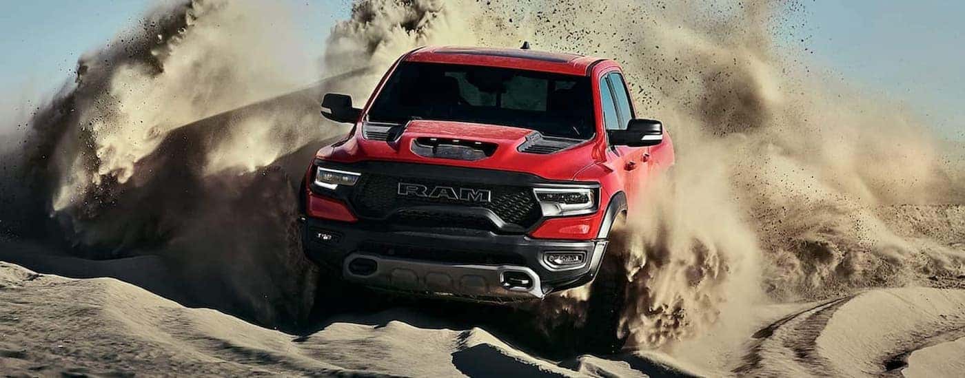 A red 2021 Ram 1500 TRX is shown driving off-road on sand.