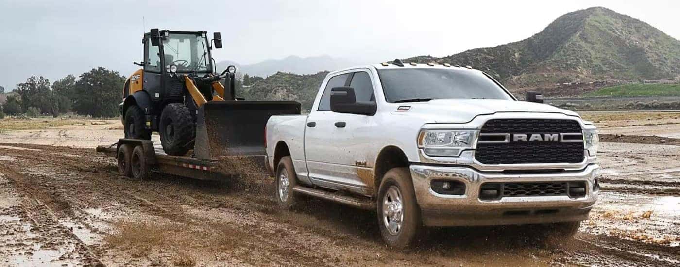 A white 2023 Ram 2500 Laramie is shown towing a towing a trailer on mud.