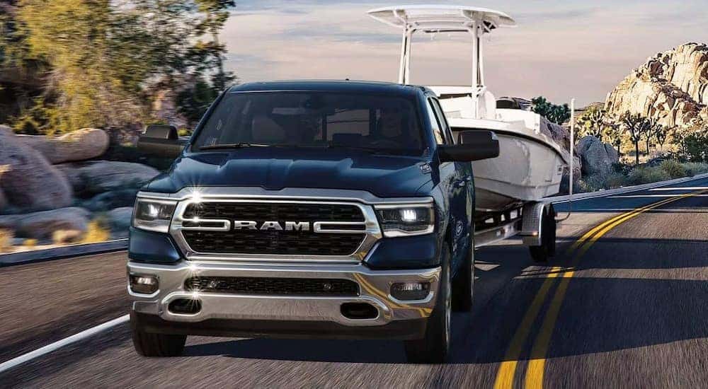 A black 2024 Ram 1500 towing a boat after visiting a dealer with a Ram 1500 for sale near Bardstown.