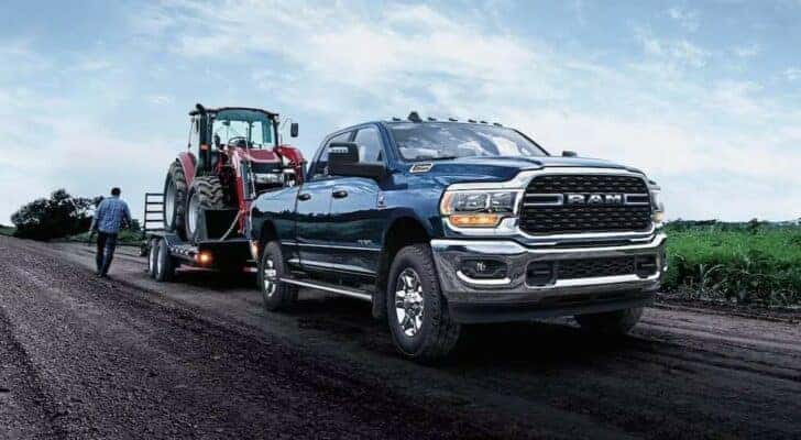A blue 2024 Ram 2500 towing a tractor.