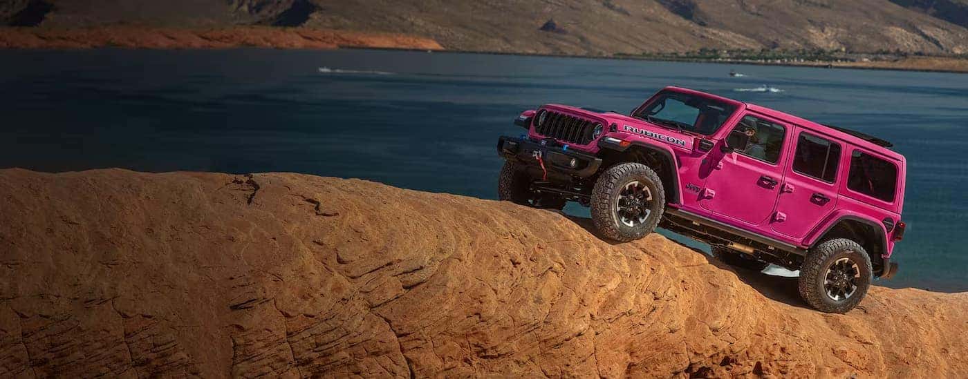 A pink 2024 Jeep Wrangler Rubicon is shown driving off-road.
