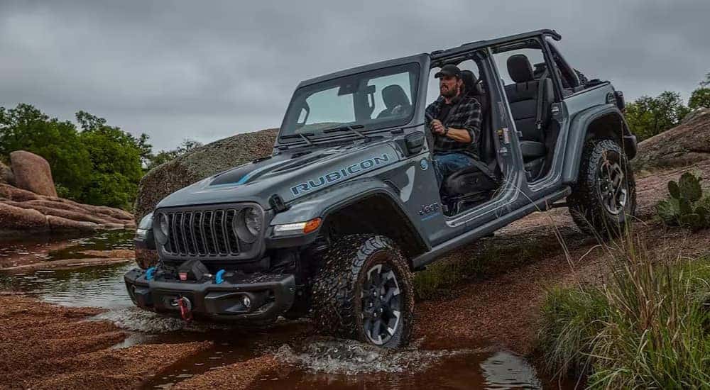 A blue 2024 Jeep Wrangler Rubicon 4xe is shown driving off-road.