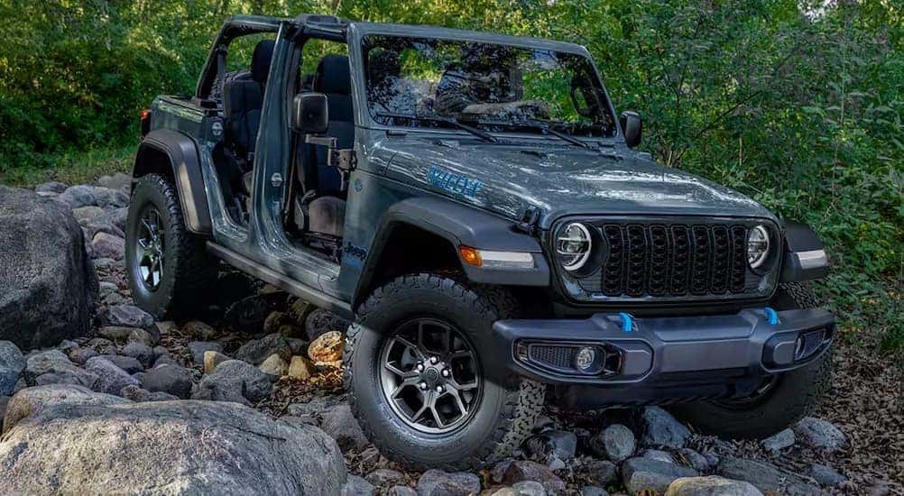 A blue 2024 Jeep Wrangler WILLYS 4xe is shown parked on rocks.