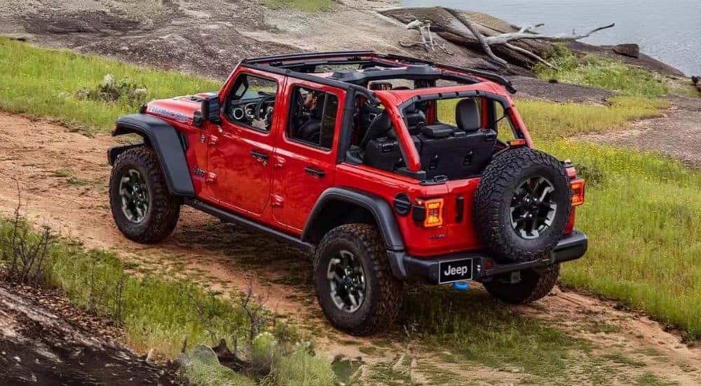 A red 2024 Jeep Wrangler 4xe is shown driving past a lake.