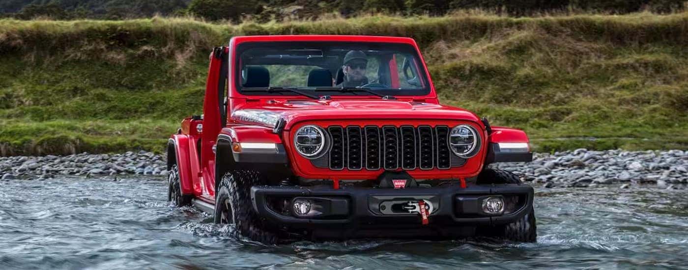 A red 2024 Jeep Wrangler Rubicon is shown driving off-road.