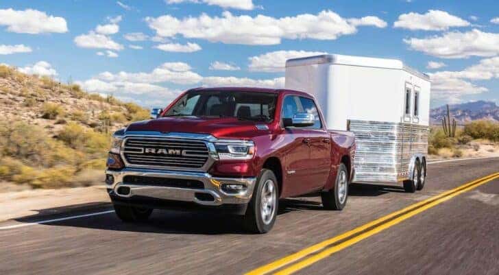 A red 2024 Ram 1500 DT is shown towing a trailer to a Ram dealer near Louisville.