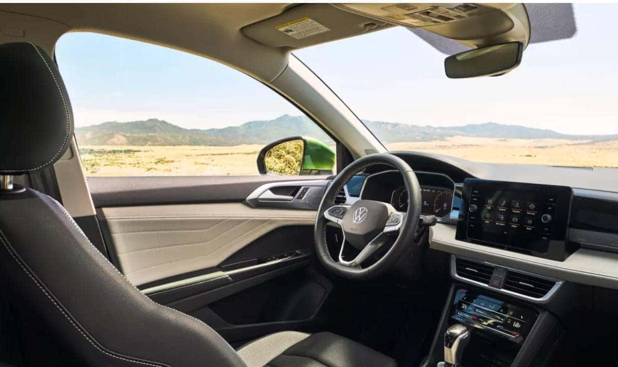 Interior view of a Volkswagen Taos dashboard, touch screen display, and desert landscape visible through the window.