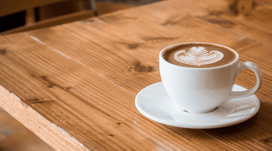 Coffee with Latte Art in White Cup and Saucer Sitting on Wood Table