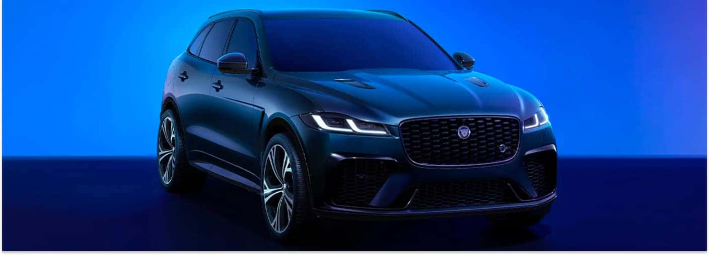 Front three-quarter view of a dark metallic green 2026 Jaguar F-PACE with headlights illuminated.