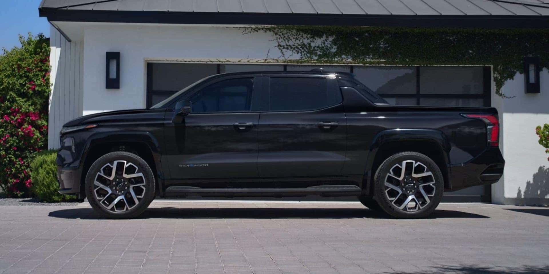 A black Chevrolet Silverado EV RST parked in a modern home driveway.