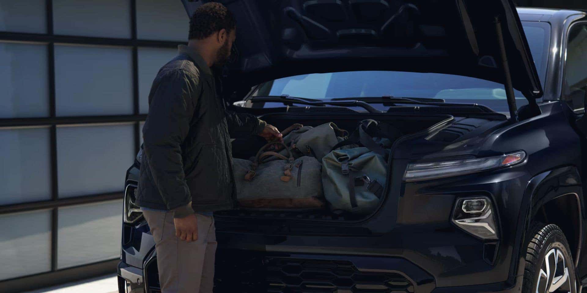 A man accessing the front trunk (frunk) storage of a Chevrolet Silverado EV, loaded with bags.