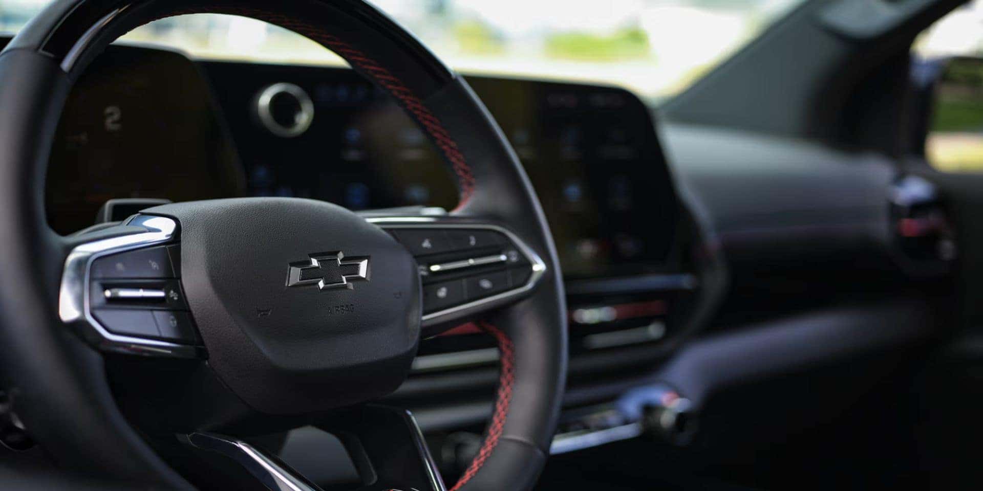Close-up of the Chevrolet Silverado EV's black interior, featuring a leather-wrapped steering wheel with red stitching.