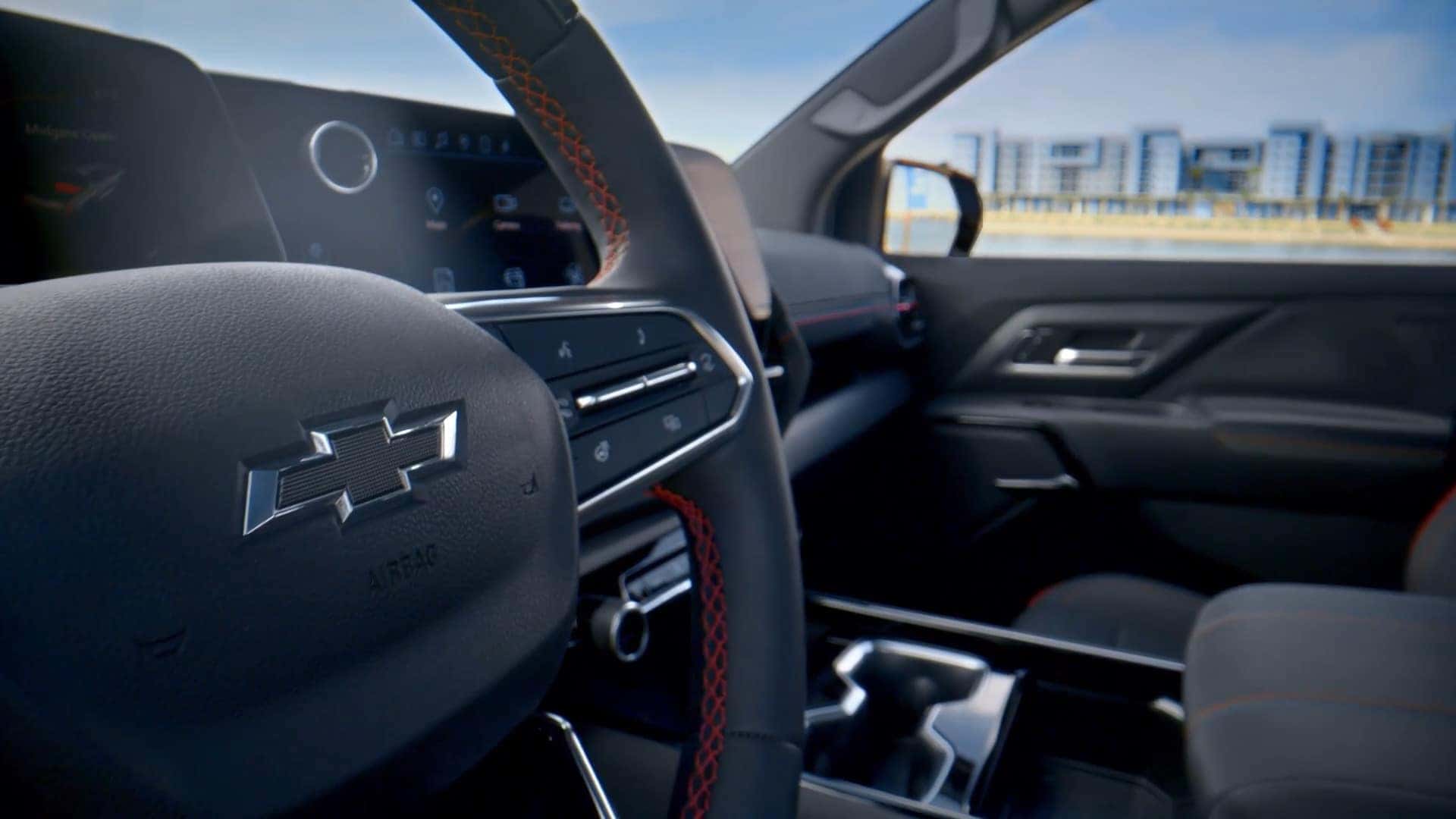 Close-up of the Chevrolet Silverado EV steering wheel with red stitching and dashboard controls.