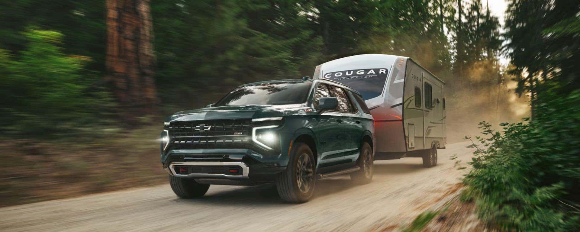 a 2025 tahoe pulling a camper on a dirt road in the woods. 